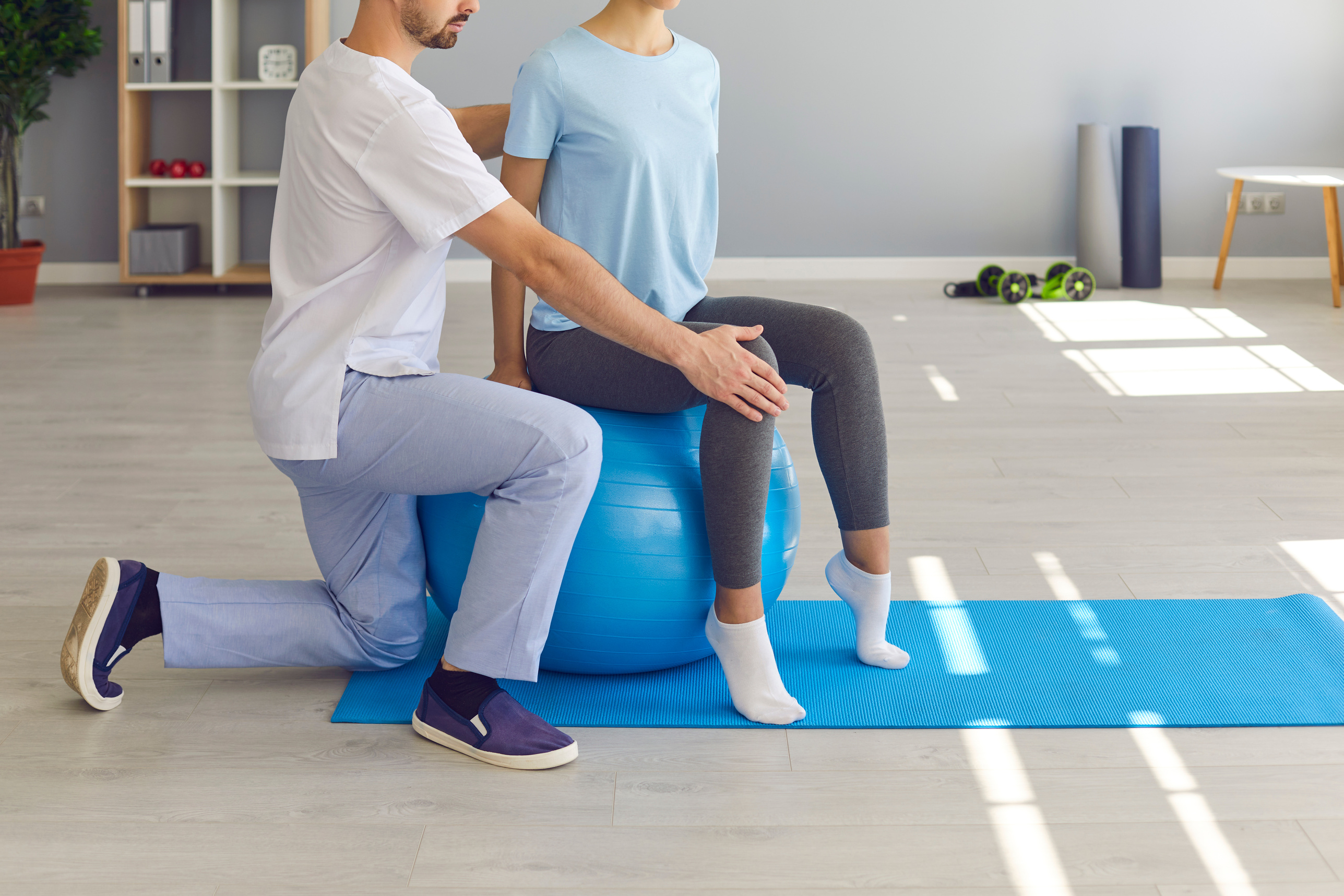 Young Woman Doing Back Fitness Exercise on Fitball with Physiotherapist or Chiropractor Helping Her